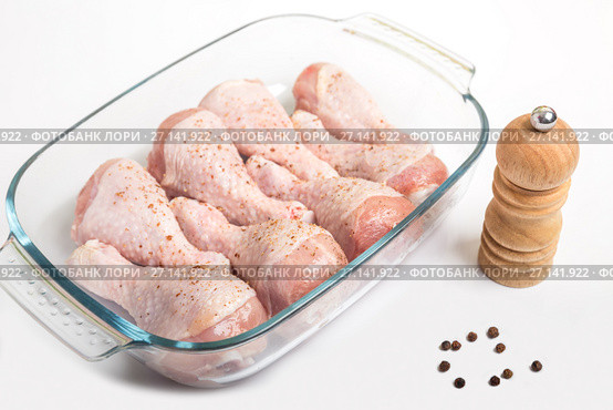 Chicken legs sprinkled with pepper in a dish for cooking on a white background. Стоковое фото, фотограф Юлия Бабкина / Фотобанк Лори