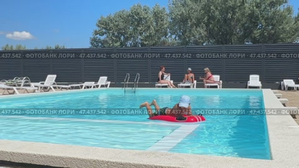 Child boy enjoys swimming in the hotel pool, while three women sit in the background, chatting and relaxing. Summer advertising of tour operators and all-inclusive hotels. Редакционное видео, видеограф Ирина Михайличенко / Фотобанк Лори
