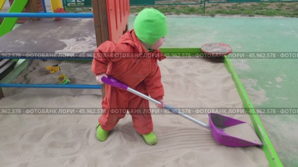 Child in orange snowsuit playing in sandbox with purple shovel. Outdoor playground scene. Winter clothing and activity concept. Стоковое видео, видеограф Андрей Журавлев / Фотобанк Лори