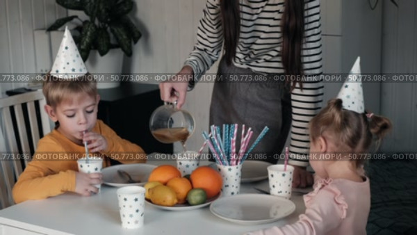 Children Drinking Juice on a Birthday Party at Home. Siblings, girls and a boy together celebrating a party, eating cake sitting at festive table. Little Kid Celebration. Surprise. Low key. Стоковое видео, видеограф Марина Демидюк / Фотобанк Лори