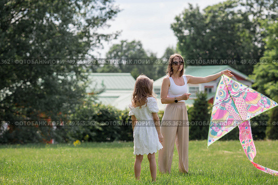 Children in the summer park. A beautiful girl and her mother are flying a kite in the fresh air. Warm family moments or a conceptual image for spending time outdoors. Стоковое фото, фотограф Photojuli / Фотобанк Лори