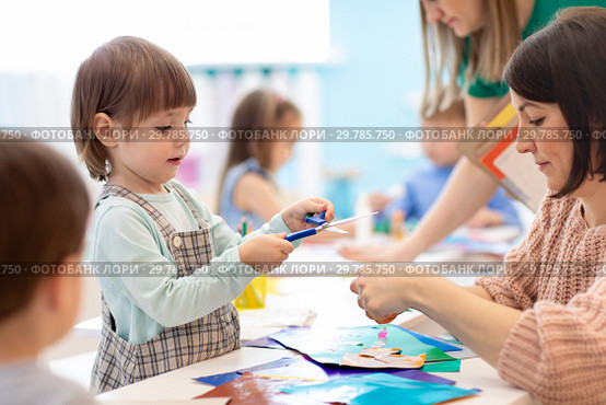 Children with scissors in hands cutting paper with teachers in class room. Group of children doing project in kindergarten. Kids play into team. Стоковое фото, фотограф Оксана Кузьмина / Фотобанк Лори