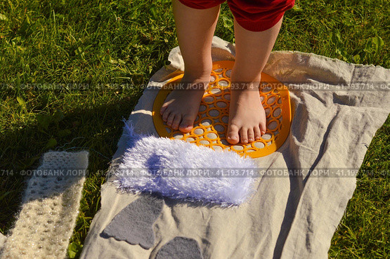 Children's feet walk on an orthopedic massage diy mat with surfaces of various shapes and tactility. grass, cones, acorns - texture details. Prevention and treatment of flat feet. Стоковое фото, фотограф Ирина Старикова / Фотобанк Лори
