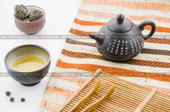 chinese clay teapot with floral blooming tea ball tea cup against white backdrop. Редакционное фото, агентство Ingram Publishing / Фотобанк Лори