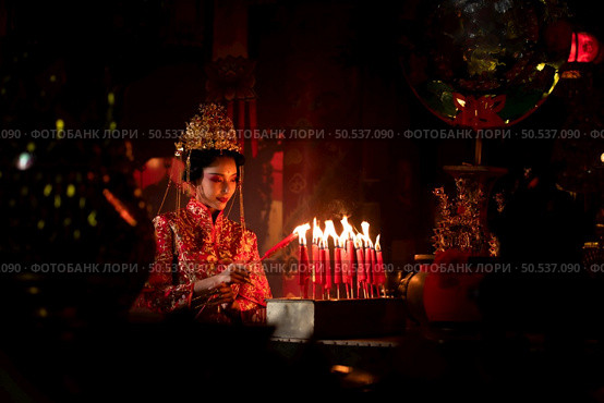 Chinese woman make wishes, pray, and light candles. On the occasion of the annual Chinese New Year festival, in a revered shrine or temple, And in Chinese where candles mean good luck and happiness. Стоковое фото, агентство Ingram Publishing / Фотобанк Лори