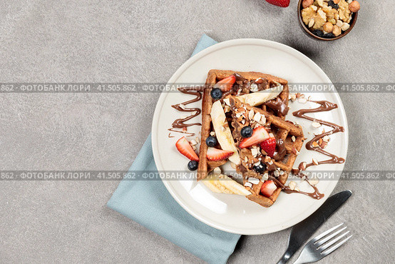 Chocolate Belgian waffles with fruits and nuts and chocolate sauce. Top view on a gray background. Стоковое фото, фотограф Bogdanova Mariia / Фотобанк Лори