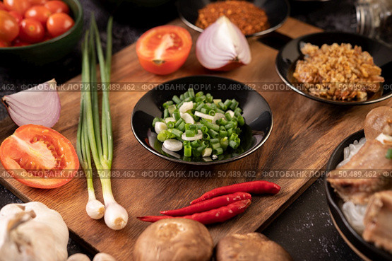 Chopped spring onion on a black plate with chili, tomatoes, and garlic. Стоковое фото, агентство Ingram Publishing / Фотобанк Лори
