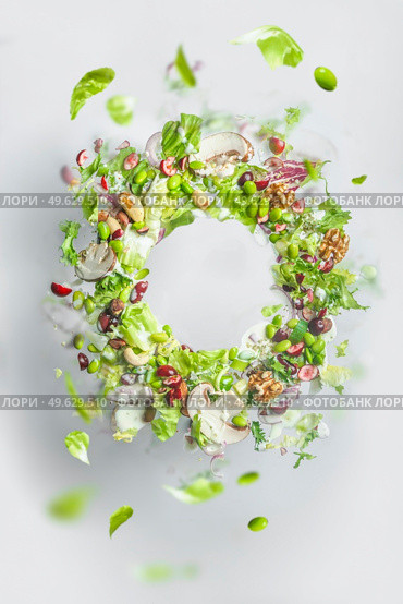 Circle frame of flying healthy green salad with lettuce, nuts, beans, dressing and vegetables. Balanced vegan food with copy space. Levitation of food. Стоковое фото, агентство Ingram Publishing / Фотобанк Лори