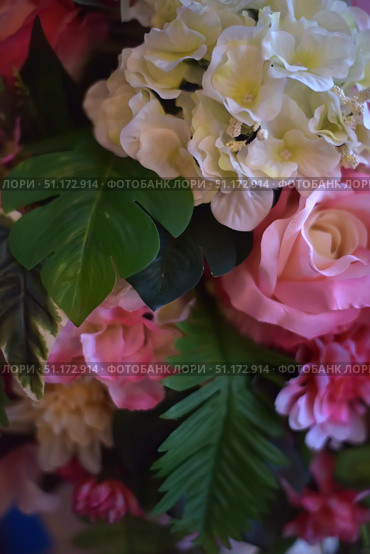 Close-up of a bright floral arrangement with green foliage. In the foreground are white flowers with yellow centers, next to them are soft pink roses and deep pink petals of decorative flowers. The contrasting green of the leaves gives the composition freshness and depth, creating a harmonious balance between light and bright shades. The photo conveys a festive and spring-like atmosphere, perfect for use in designs dedicated to weddings, romantic events, interior decor and floral projects. Стоковое фото, фотограф Анна Кривицкая / Фотобанк Лори