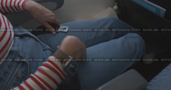 Close-up of female hands fastening and unfastening seat belt on airplane seat during flight, woman demonstrates safety procedures for passengers on board commercial aircraft, travel safety concept. Стоковое видео, видеограф Сергей Тимофеев / Фотобанк Лори