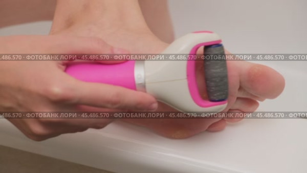 Close-up of person using an electric foot file to remove calluses from the foot. Personal care and hygiene concept. Design for healthcare, beauty, and skincare promotion. A woman of 40 years old. Стоковое видео, видеограф Андрей Журавлев / Фотобанк Лори