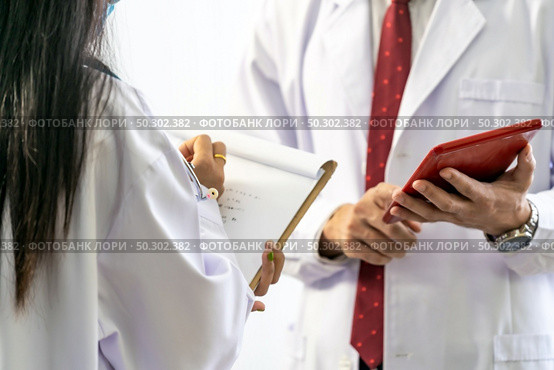 close up of senior doctor giving his younger colleagues a piece of advice concerning the diagnosis in clinic hospital. Healtcare teamwork concept. Стоковое фото, агентство Ingram Publishing / Фотобанк Лори