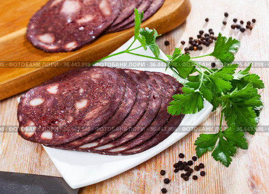 Close up of Spanish smoked blood sausage on white plate on wooden table. Стоковое фото, фотограф Яков Филимонов / Фотобанк Лори