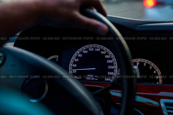 Close up of Twilight Drive With Focus on Speedometer and Steering Wheel. Close-up of cars speedometer, drivers hand on steering wheel during an evening drive. Car transport concept. Copy ad text space. Стоковое фото, фотограф Aleksandr Golubev / Фотобанк Лори