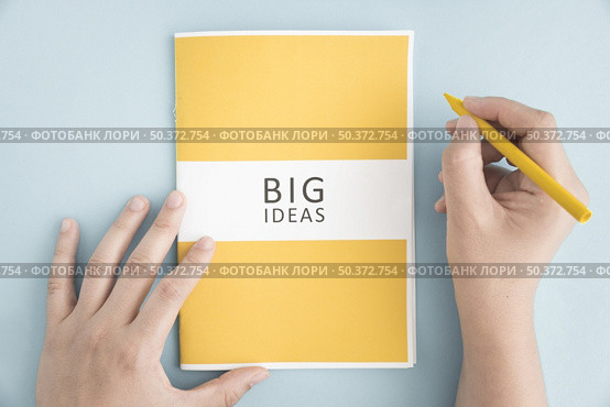 close up person holding yellow crayon with big idea book blue background . Стоковое фото, агентство Ingram Publishing / Фотобанк Лори