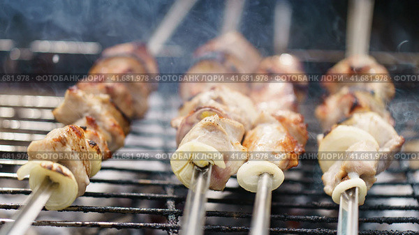 Closeup image of cooking delicious barbecue, shish kebabs with onion on the grill with coals. Appetizing pieces of meat are fried on metal skewers. Holidays in the nature. Tasty picnic in forest. Стоковое фото, фотограф YuryKara / Фотобанк Лори