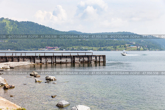 Coast of Baikal Lake on summer day. View of wooden pier in village of Port Baikal on shore of  lake. In distance beyond Angara River, village of Listvyanka is visible. Beautiful landscape. Nature background. Стоковое фото, фотограф Виктория Катьянова / Фотобанк Лори