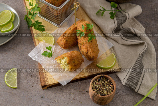 Cod dumplings, or "bolinhos de bacalhau" and parsley leaves and lemons on wooden cutting board in a kitchen counter top. Стоковое фото, агентство Ingram Publishing / Фотобанк Лори