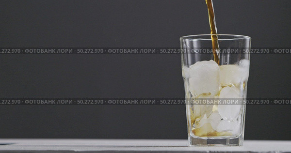 Coffee is poured into a transparent glass with ice making bulbs around a dark background. Slow motion, 2K UHD video, 240fps, 1080p.. In a glass with ice pour coffee with splashes and bulbaki around dark background. Стоковое фото, агентство Ingram Publishing / Фотобанк Лори