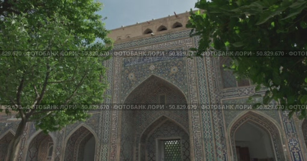 Colorful facade of Islamic madrasa with intricate geometric mosaics and traditional oriental architecture in Samarkand Uzbekistan under blue sky, arched entrance, tile ornament with Arabic calligraphy. Стоковое видео, видеограф Сергей Тимофеев / Фотобанк Лори