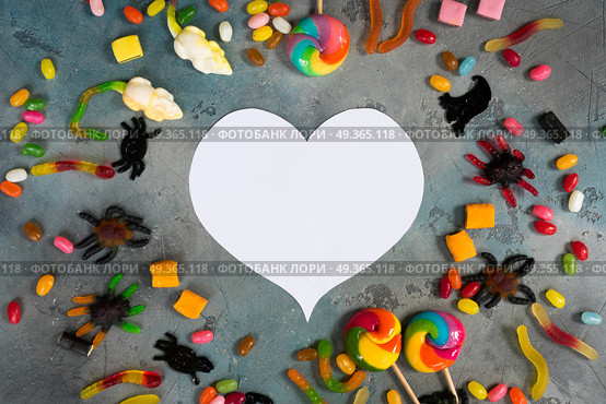 Colorful halloween candies on stone. Trick and treat - colorful halloween candies flat lay scene on stone with copy space on white heart. Стоковое фото, агентство Ingram Publishing / Фотобанк Лори