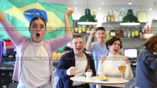 Company of enthusiastic young adult sports fans waving flag of Brazil and supporting national team with beer in pub. Стоковое видео, видеограф Яков Филимонов / Фотобанк Лори