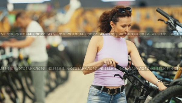 Confident stylish modern woman thoughtfully comparing bicycle models in shop, considering handlebar system, while picking perfect bike for fitness and travel. Стоковое видео, видеограф Яков Филимонов / Фотобанк Лори