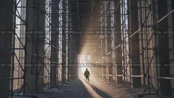 Construction worker wearing safety vest and hardhat walking through scaffolding on building site at sunset, representing construction industry, engineering, and development. Стоковое AI-видео, аниматор Данил Руденко / Фотобанк Лори