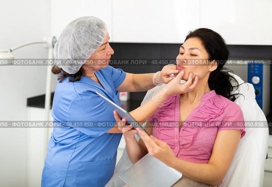 Cosmetologist planning upcoming lip reshaping procedures for female patient. Стоковое фото, фотограф Яков Филимонов / Фотобанк Лори