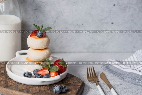 Cottage cheese pancakes, Russian cheesecakes with fresh blueberries, strawberries and mint on a stylish wooden board on a gray concrete table. Natural products. Healthy and delicious breakfast. Стоковое фото, фотограф Photojuli / Фотобанк Лори
