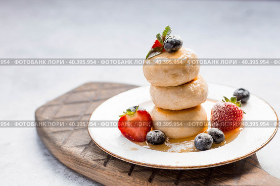 Cottage cheese pancakes, Russian cheesecakes with fresh blueberries, strawberries, honey and mint leaves on a stylish wooden board on a gray concrete table. Natural products. Healthy and delicious breakfast. Стоковое фото, фотограф Photojuli / Фотобанк Лори