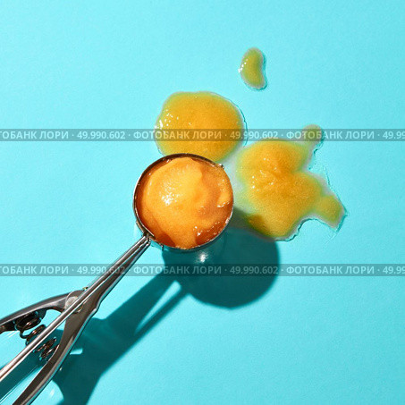 Creative composition from a ball of yellow ice cream on a metal spoon on a blue glass background with shadows. Food modern style.. Flat lay of a spoon for ice cream with yellow mango dessert and melted ice cream on a blue background with hard shadows. Стоковое фото, агентство Ingram Publishing / Фотобанк Лори
