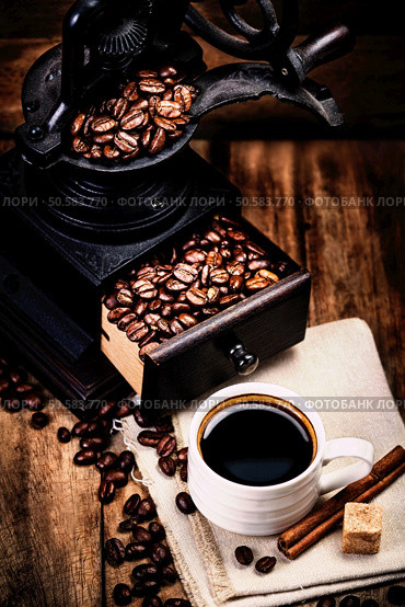 Cup of coffee with coffee beans and Coffee grinder on wooden brown background closeup.  Espresso Cup on brown napkin with cinnamon sticks  and sugar.. Cup of coffee with coffee beans and Coffee grinder on wooden brown background closeup.  Espresso Cup on brown napkin with cinnamon . Стоковое фото, агентство Ingram Publishing / Фотобанк Лори