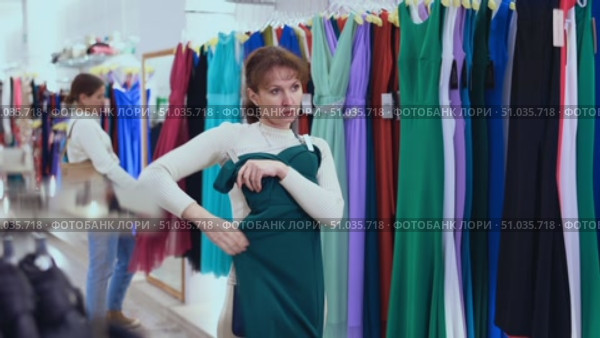 Customer in store has removed hanger with floor-length gown from window and is considering product. Woman client imagines successful new summer outfit. Стоковое видео, видеограф Яков Филимонов / Фотобанк Лори