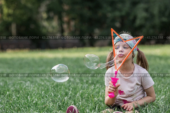 Cute happy girl playing with soap bubbles on a summer day. A child in the fresh air, in nature. The concept of a happy childhood and a holiday. Стоковое фото, фотограф Photojuli / Фотобанк Лори
