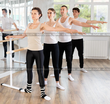 Dancing positive women and men engaged in group class perform exercise near ballet barre, standing in 2nd position of ballet stance in dance studio. Стоковое фото, фотограф Яков Филимонов / Фотобанк Лори