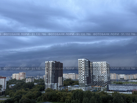 Dark, heavy clouds hang low over a modern city with residential buildings and green trees. Concept of: Impending weather. Стоковое фото, фотограф Ольга Петрова-Апостолова / Фотобанк Лори