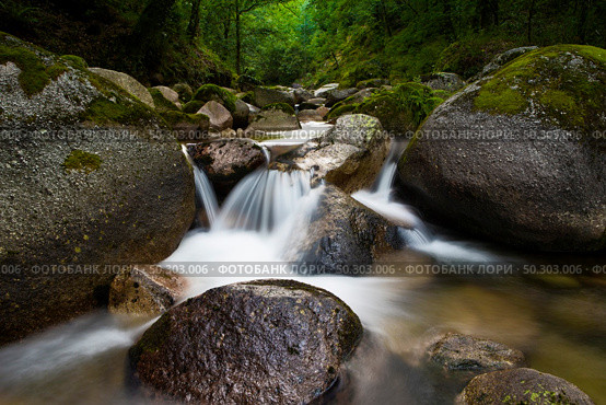Dark rapid stream with bright blurred blue waves. Big mossy boulders in clear water of mountain river. Стоковое фото, агентство Ingram Publishing / Фотобанк Лори