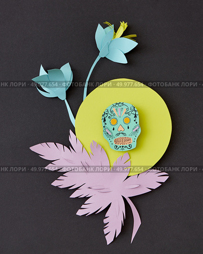Decorative handcraft composition from paper with flowers, leaf and skull on a yellow round frame on black paper background, copy space. Calaveras attribute of the Mexican holiday of Calaca. Flat lay. Greeting card with Calaveras skull, decorated paper flowers calendula, leaf and creative on a yellow frame on a black paper. Стоковое фото, агентство Ingram Publishing / Фотобанк Лори