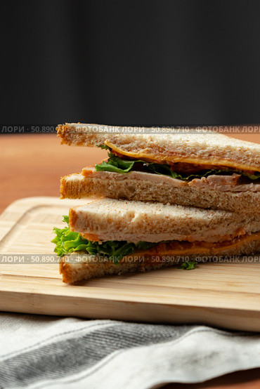 Delicious layered sandwich with lettuce and cheese served on a wooden board in a cozy setting. Стоковое фото, фотограф Сергей Толмачёв / Фотобанк Лори