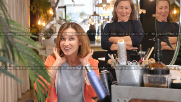 Delighted young female client sitting in hairdressing chair after haircut from professional stylist. Стоковое видео, видеограф Яков Филимонов / Фотобанк Лори