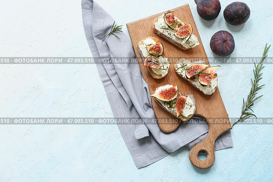 Деревянная доска с вкусной брускеттой из инжира с рикоттой и розмарином на светло-голубом фоне. Стоковое фото, фотограф Pixel_shot / Фотобанк Лори