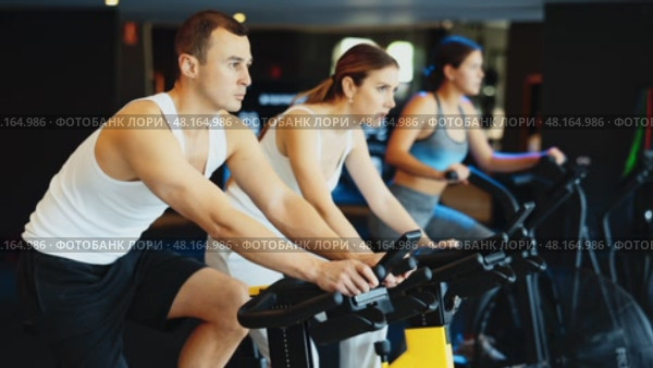 Determined young guy training with spin bike in fitness hall during full-body workout. Стоковое видео, видеограф Яков Филимонов / Фотобанк Лори
