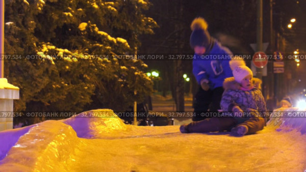 Дети катаются с ледяной горки на городской площади. Children ride on an ice slide in the town square. (2019 год). Редакционное видео, видеограф Евгений Романов / Фотобанк Лори