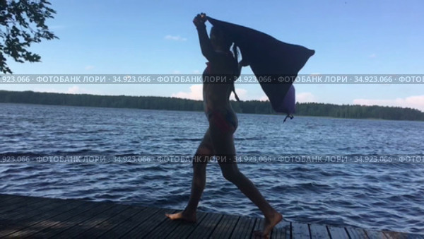 Девочка идет по причалу с развевающимся на ветру полотенцем, замедленное видео. Стоковое видео, видеограф Кекяляйнен Андрей / Фотобанк Лори
