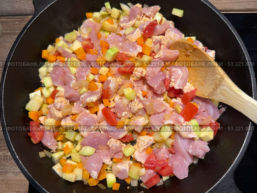 Diced chicken and vegetables are being stir-fried in a cast-iron pan with a wooden spoon. Concept of: Culinary preparation. Стоковое фото, фотограф Ольга Петрова-Апостолова / Фотобанк Лори