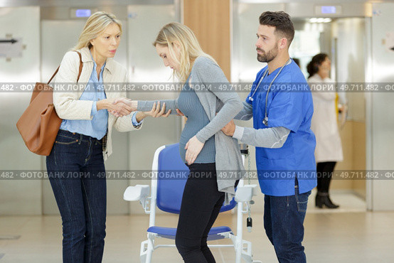 doctor helping pregnant woman to sit down on wheelchair. Стоковое фото, агентство Ingram Publishing / Фотобанк Лори