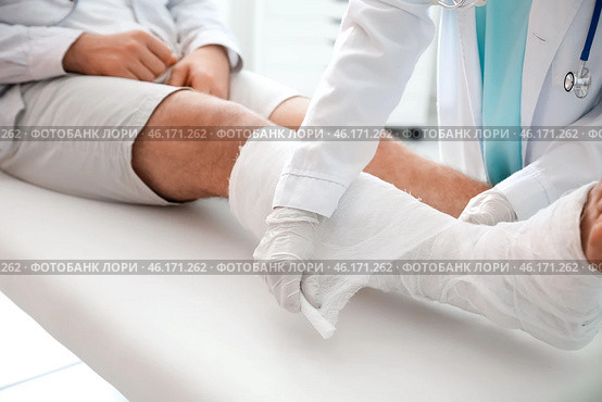 Doctor putting broken leg of young man in plaster. Стоковое фото, фотограф Pixel_shot / Фотобанк Лори
