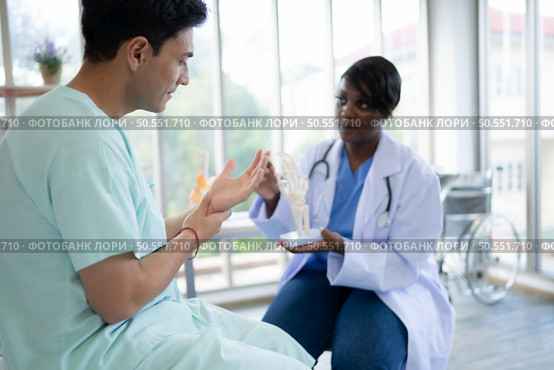 Doctor showing model of finger bones to patient in hospital. Medical and healthcare concept. Стоковое фото, агентство Ingram Publishing / Фотобанк Лори