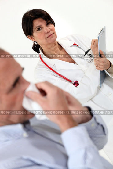 Doctor writing on a clipboard as her patient blows his nose. Стоковое фото, агентство Ingram Publishing / Фотобанк Лори